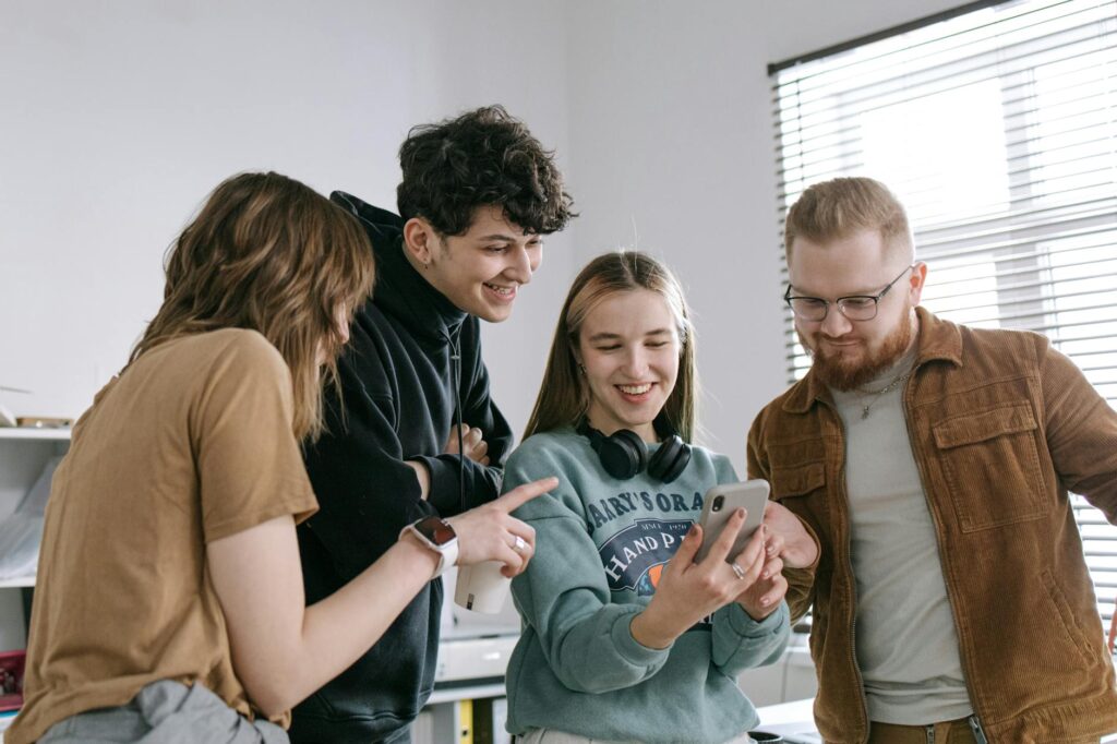 group of people smiling while looking at woman s mobile phone